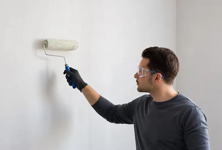 Процесс косметического ремонта маляр валиком красит стену в спальне